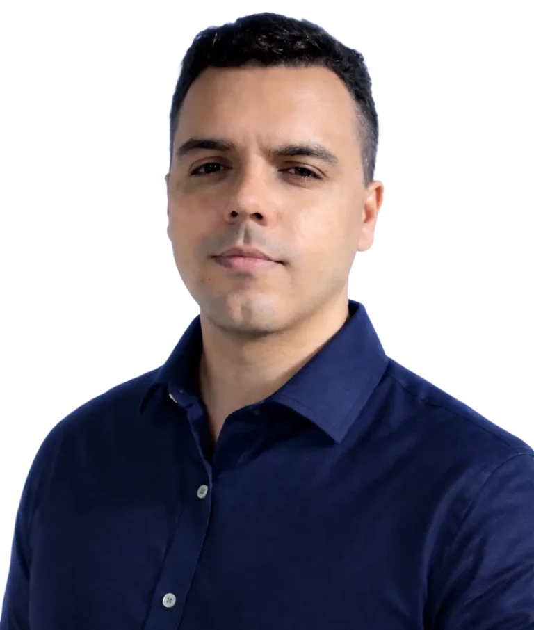 Homem jovem de pele morena e cabelos curtos escuros, vestindo uma camisa social azul marinho, posando para um retrato corporativo contra um fundo branco limpo.